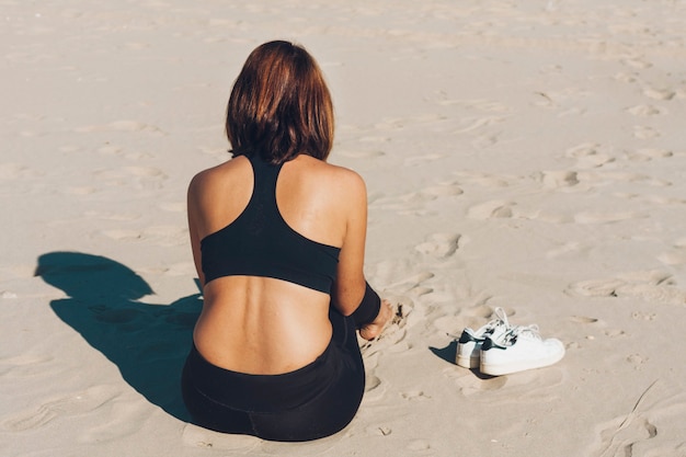 femme assise sur le sable à côté de chaussures de sport