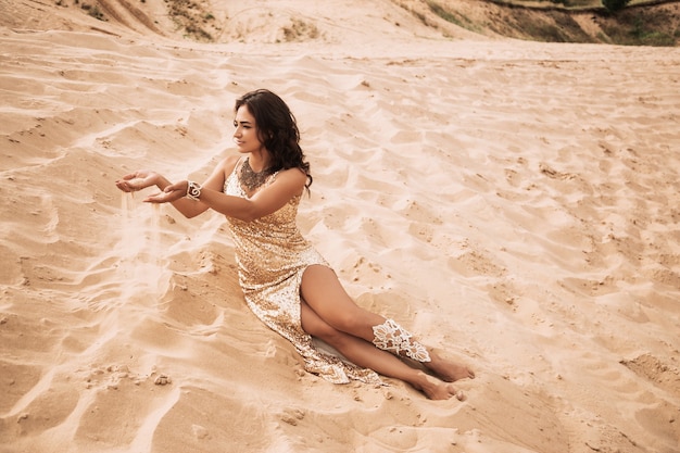 Femme assise sur le sable du désert et tenant le sable à la main.