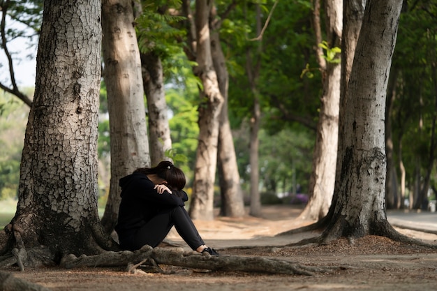 Femme assise seule et triste avec son visage entre ses bras dans le sol du parc