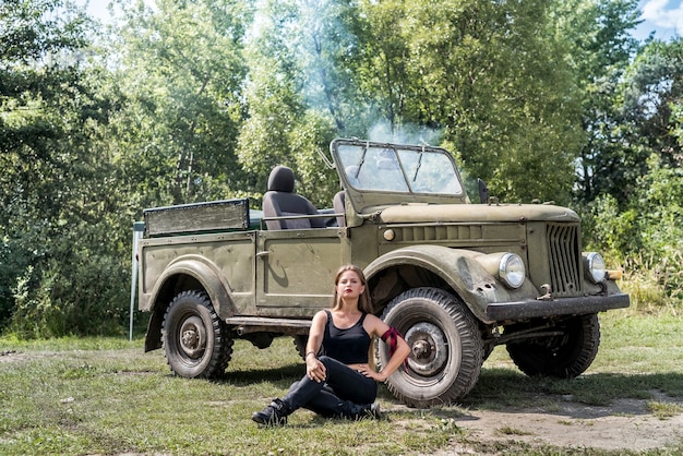 Photo femme assise sur le sol près de la voiture militaire