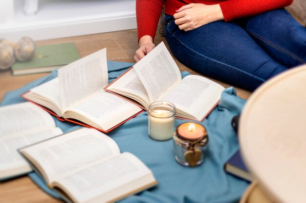 Femme assise sur le sol de sa maison en hiver lisant plusieurs livres aux chandelles