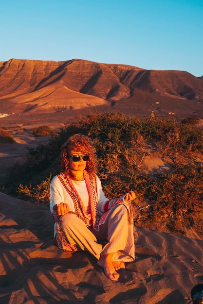 Femme assise sur le sol de sable et méditant en position de yoga loto et vêtements décontractés Équilibre intérieur et sentiment avec le mode de vie de concept de nature en plein air Adultes profitant du soleil et d'un mode de vie sain