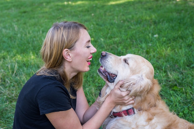 Une femme assise sur le sol avec son chien retriever sur l'herbe. La femme joue et fait des grimaces avec le chien.