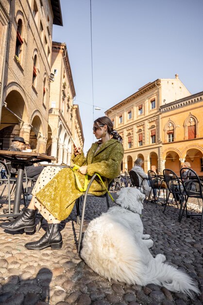 Femme assise avec son chien blanc au café en plein air dans la vieille ville de Bologne