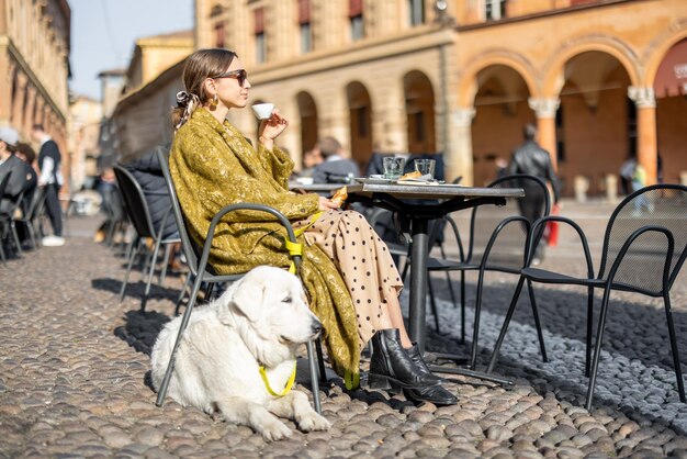 Femme assise avec son chien blanc au café en plein air dans la vieille ville de Bologne