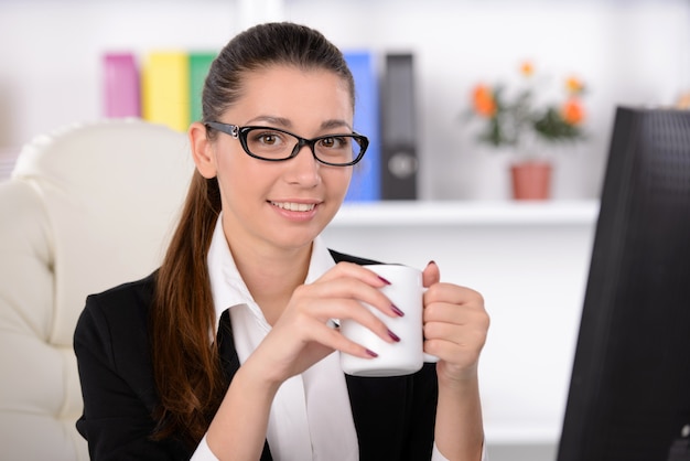 Femme assise sur son lieu de travail et buvant du café.