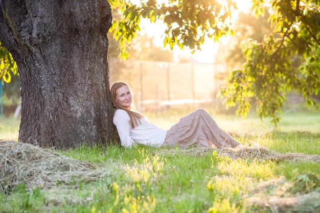 Femme assise sous l'arbre et regardant le coucher du soleil