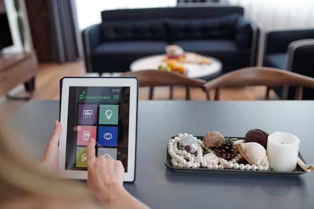 Femme assise à table dans le salon et verrouillant la porte de l'appartement via une application sur une tablette