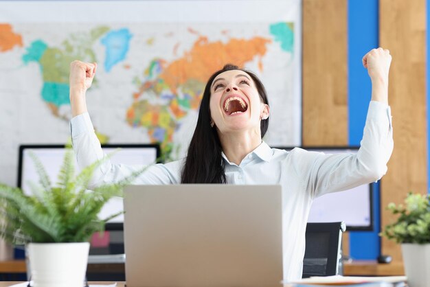 Femme assise à table devant l'ordinateur heureuse de terminer la tâche de l'entreprise pour réussir le test