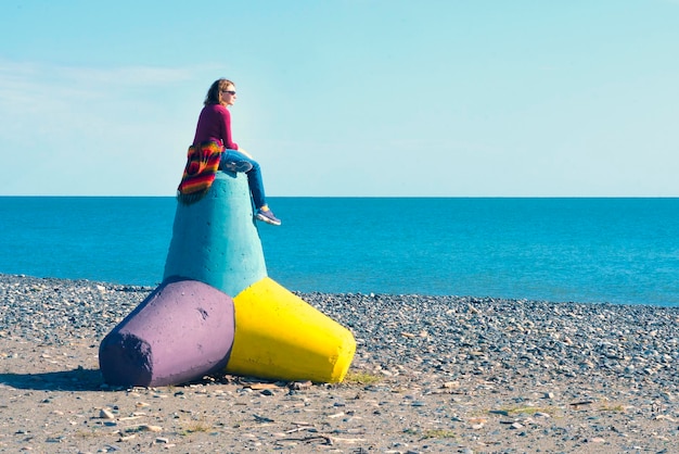 Femme assise sur un tétrapode en béton sur la plage