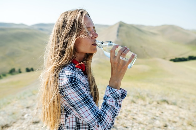 Femme assoiffée de l'eau potable. Épuisé par la randonnée. Entouré de belles collines herbeuses, s'étendant loin.