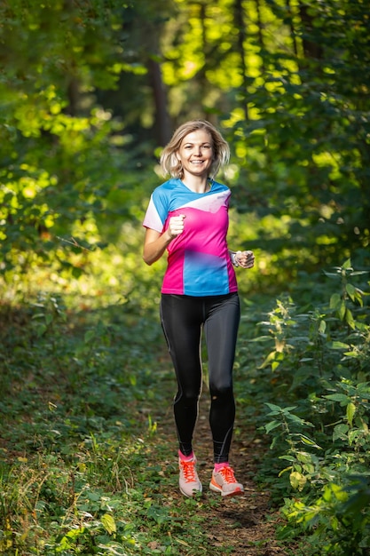 Femme d'athlète de remise en forme qui traverse le parc parmi les arbres le matin d'été.