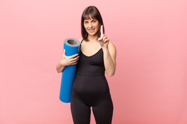 Femme athlète souriante fièrement et avec confiance faisant triomphalement la pose numéro un, se sentant comme un leader