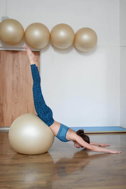 Une femme athlétique caucasienne entraîne son équilibre sur un fitball dans la salle de gym