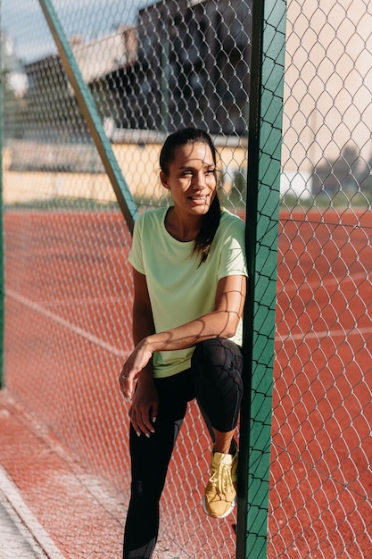 Femme athlétique debout près de grillage au stade