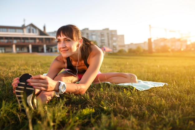 Femme Athlétique étirant Ses Ischio-jambiers, Les Jambes Exercent L'entraînement Physique Avant L'entraînement à L'extérieur Avec Un Casque D'écoute De Musique.