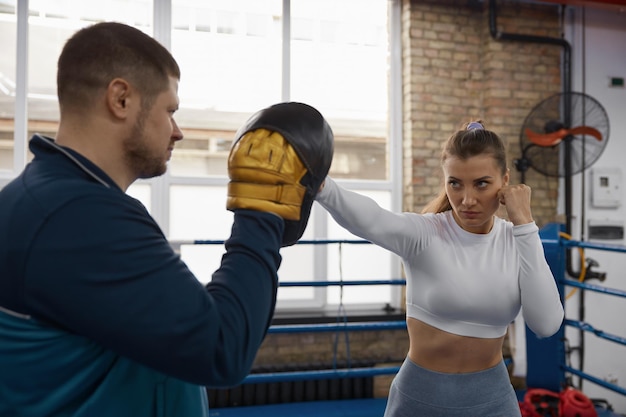 Une femme athlétique frappe un entraîneur sur une leçon d'entraînement de taebo au gymnase.