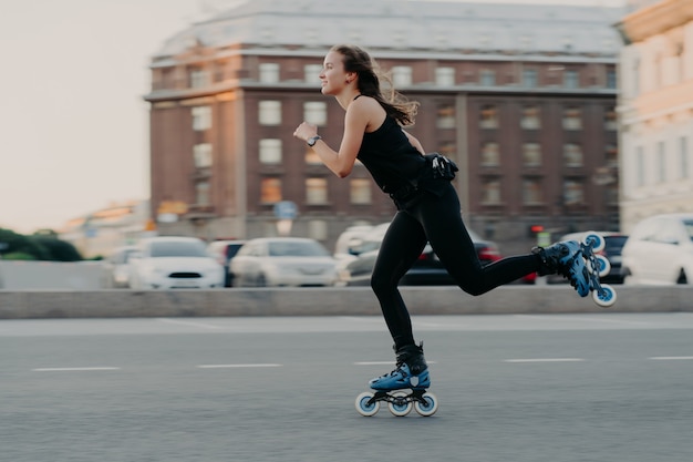 Une femme athlétique monte sur des rouleaux se déplace très rapidement vêtue de vêtements de sport aime faire du patin à roues alignées photographiée dans des poses d'action dans un lieu urbain engagé dans un sport extrême. Concept de mode de vie actif