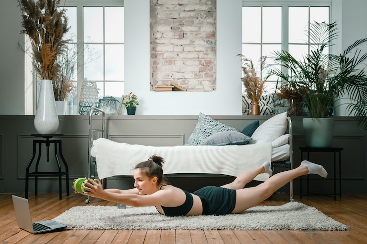 Photo femme athlétique positive avec des cheveux bien attachés et des vêtements de sport serrés tient la planche avec des haltères sur le sol à la maison.