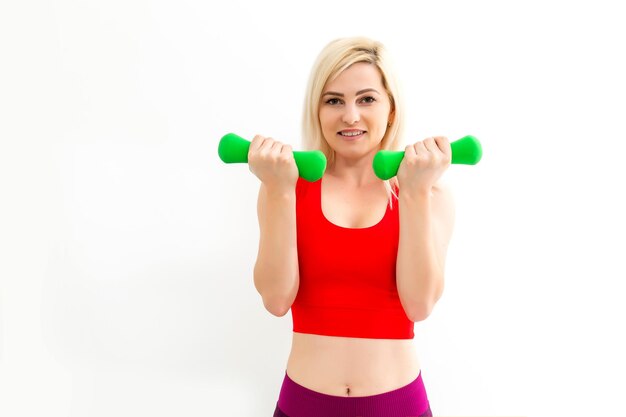 Femme athlétique souriante, pomper les muscles avec des haltères sur fond blanc