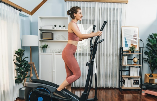 Une femme athlétique et sportive courant sur une machine de course elliptique à la maison de gaieté