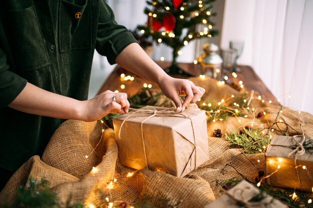 Femme attachant la boîte-cadeau d'artisanat de vacances avec des branches d'épinette sur la table en bois