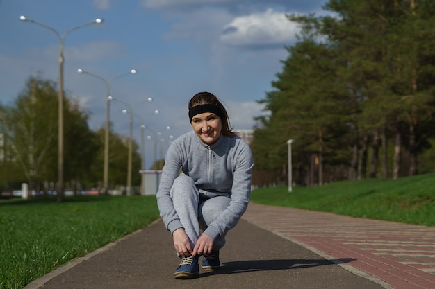 Femme attachant des lacets de chaussures. Coureur de fitness sportif féminin se préparant à faire du jogging à l'extérieur sur un chemin forestier au printemps ou en été.