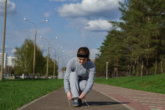 Femme attachant des lacets de chaussures. Coureur de fitness sportif féminin se préparant à faire du jogging à l'extérieur sur un chemin forestier au printemps ou en été.