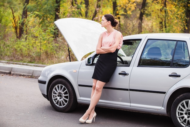 Une femme attend de l'aide près de sa voiture en panne sur le bord de la route