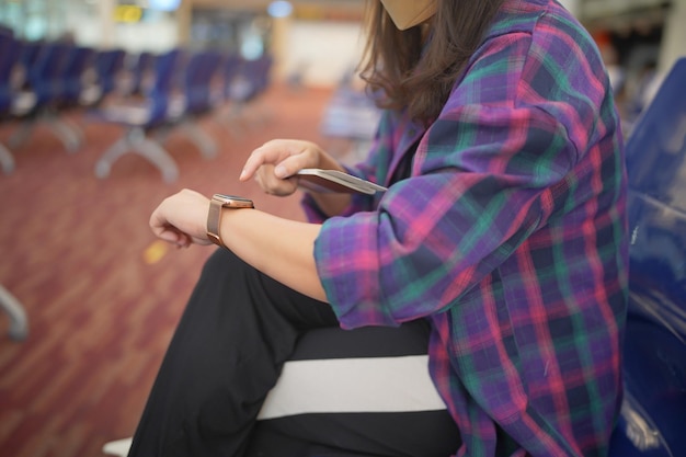 Femme attendant le départ à l'aéroport pendant vos vacances, détenez un passeport et un smartphone en attendant l'embarquement dans la zone de départ de l'aéroport international