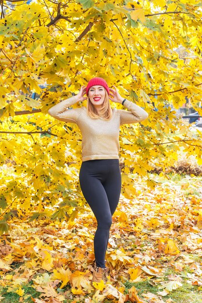 Femme au bonnet rouge parmi les feuilles d'automne jaunes. Femme posant près d'un érable dans le parc