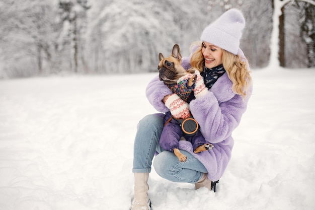 Femme au bonnet tricoté jouant avec son chien bouledogue français sur une neige