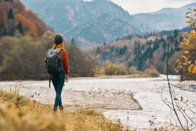 Femme au bord de la rivière dans les montagnes dans la forêt d'automne dans la nature vue arrière