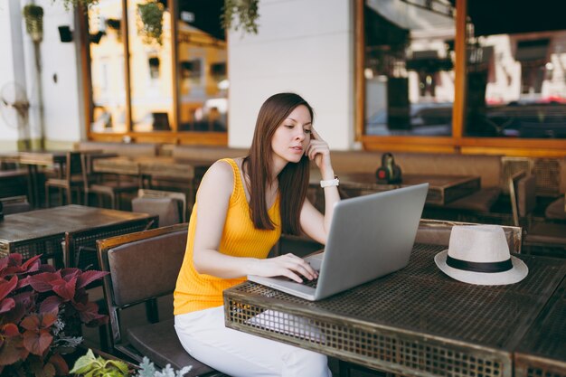 Femme au café de la rue en plein air assis à table travaillant sur un ordinateur portable moderne, se relaxant au restaurant pendant le temps libre