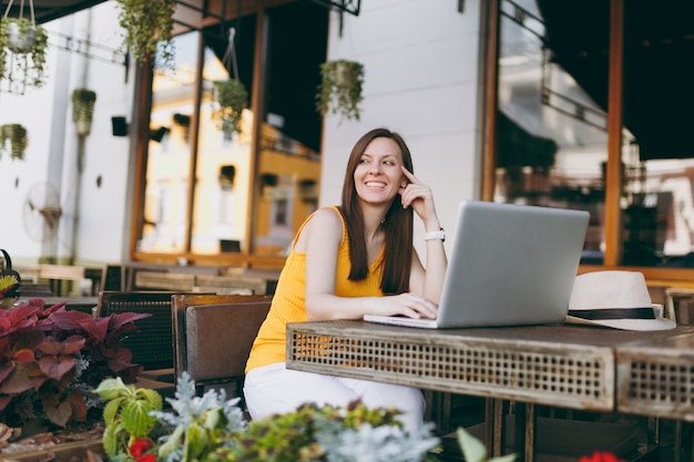 Femme au café de la rue en plein air assis à table travaillant sur un ordinateur portable moderne, se relaxant au restaurant pendant le temps libre