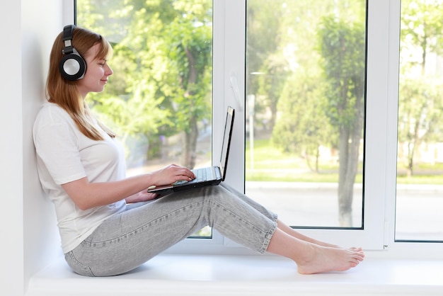 Femme au casque et ordinateur portable sur la fenêtre