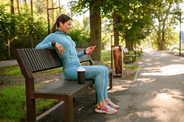 Femme au casque se détendre sur un banc après l'entraînement du matin dans le parc