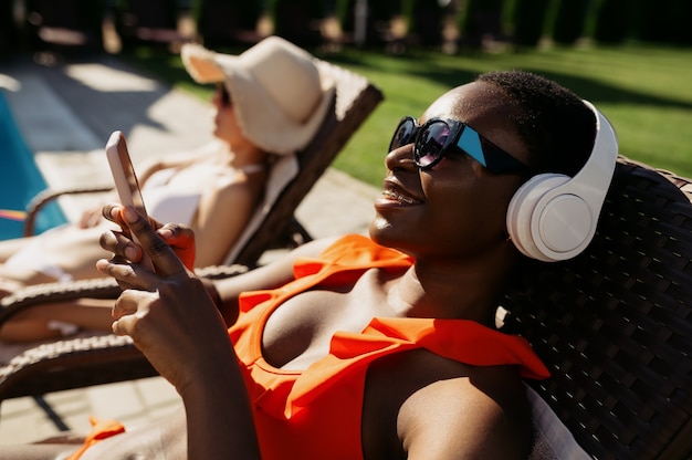 Femme au casque en train de bronzer sur un transat au bord de la piscine