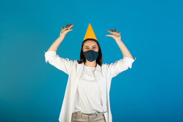 Femme au chapeau d'anniversaire jaune et masque médical fête son anniversaire pendant le temps du coronavirus.
