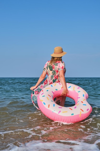 Femme au chapeau et bikini nageant sur un anneau de beignet gonflable