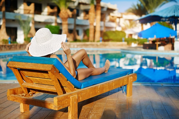 Femme au chapeau blanc allongé sur une chaise longue près de la piscine à l&#39;hôtel