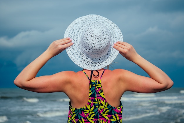 Femme au chapeau blanc regarde la mer