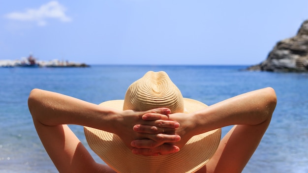 Femme au chapeau est allongée sur une chaise longue sur la plage au bord de la mer