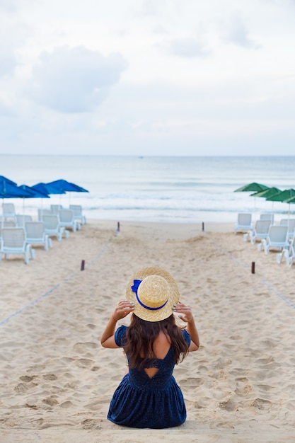 Femme au chapeau est assise sur une plage de sable