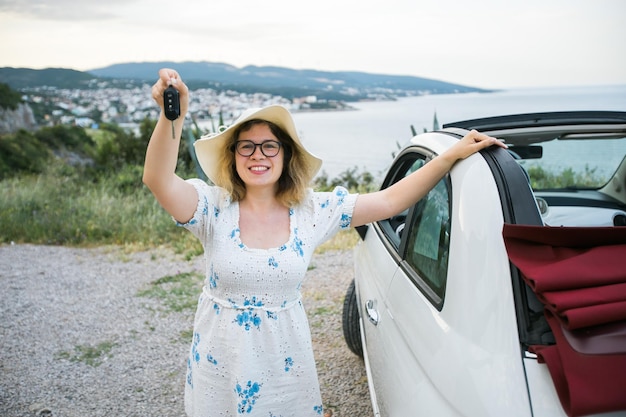 Femme au chapeau d'été chauffeur tenant les clés de voiture au volant de sa nouvelle voiture cabriolet automobile et achat co