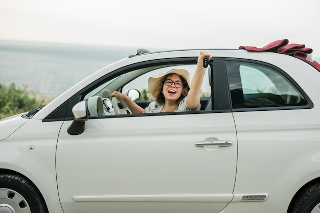 Femme au chapeau d'été chauffeur tenant des clés de voiture conduisant sa nouvelle voiture cabriolet automobile et concept d'achat