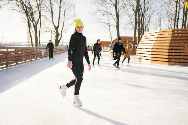 Une femme au chapeau jaune patine sur une patinoire en hiver