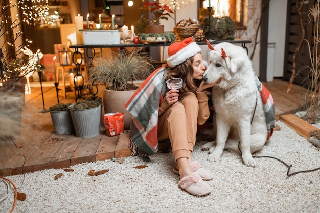 Femme au chapeau de noël célébrant avec son chien mignon les vacances du Nouvel An, assis ensemble sur la terrasse joliment décorée à la maison