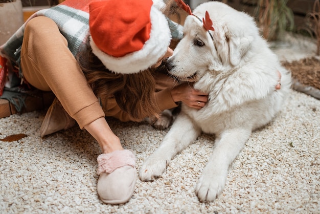 Femme au chapeau de noël célébrant avec son chien mignon les vacances du Nouvel An, assis ensemble sur la terrasse joliment décorée à la maison