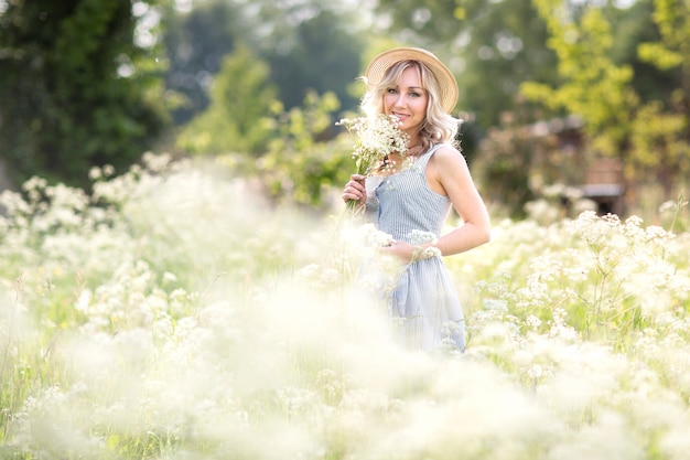 Femme au chapeau de paille dans un champ de fleurs avec un bouquet de fleurs sauvages